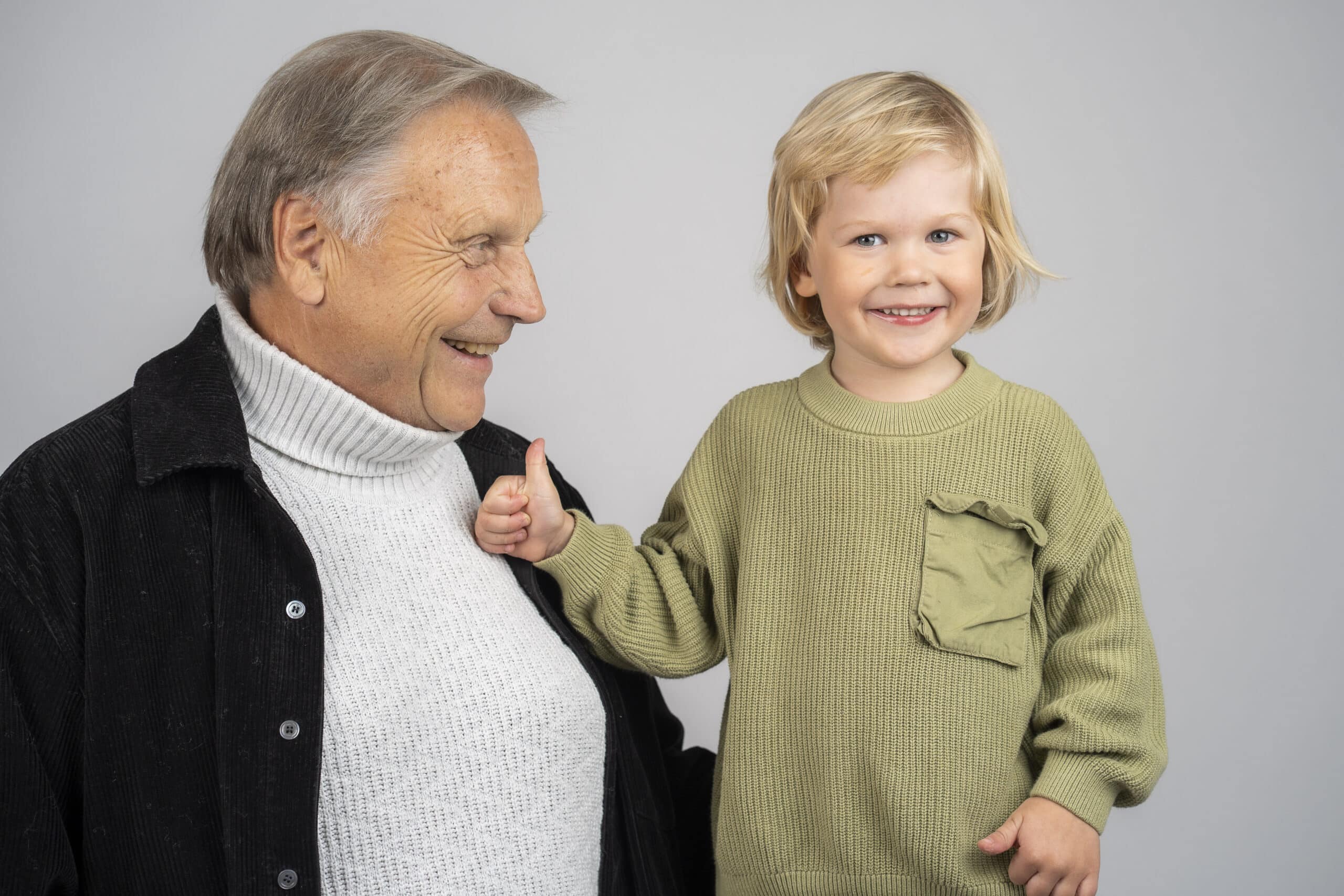 Vanhempi mies ja lapsi vierekkäin. Mies katsoo lasta hymyillen ja lapsi katsoo kameraan hymy naamallaan.