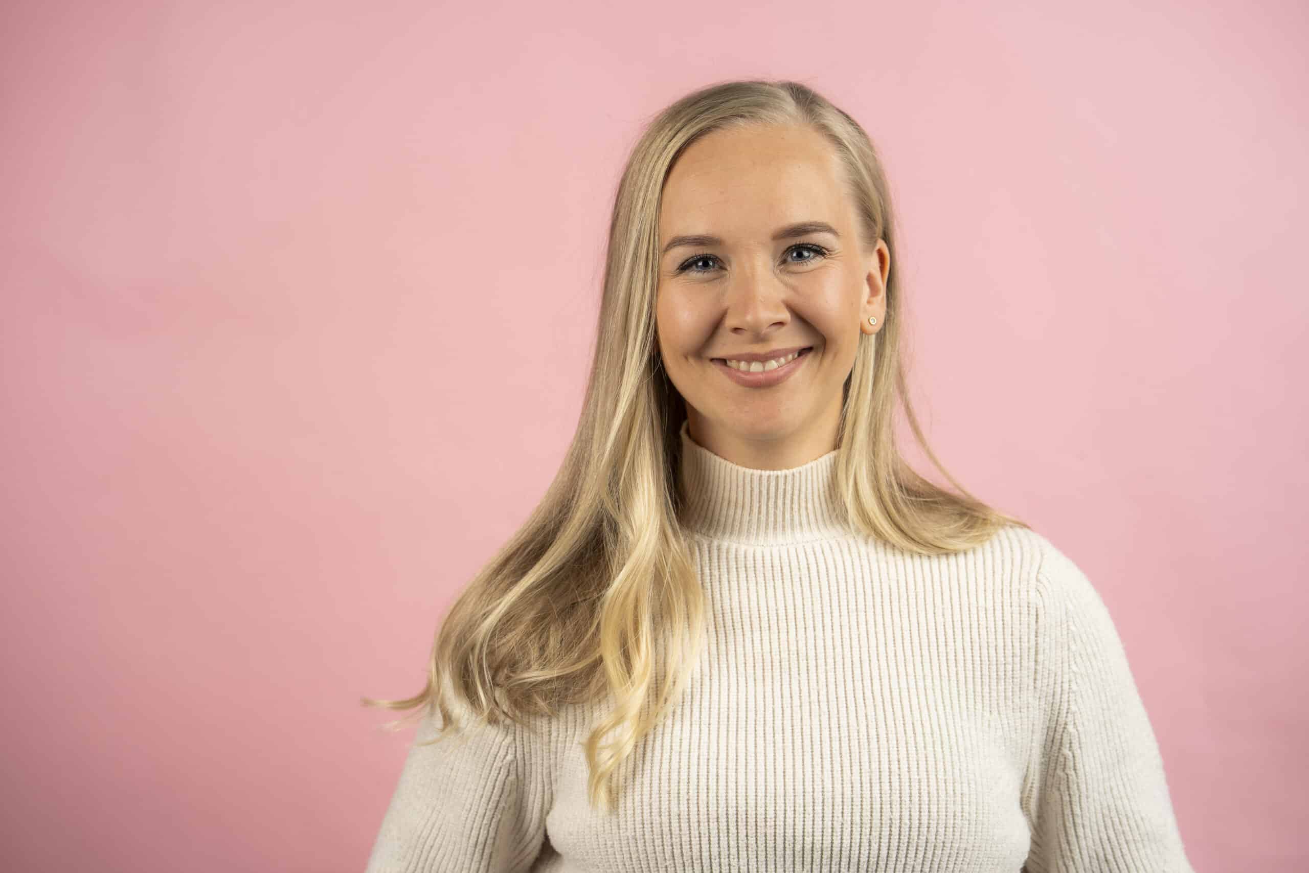 Hampaiden oikominen, oikomishoito kansikuva DentÅ. NAinen hymyilee kameralle, vaaleanpunainen studiotausta.